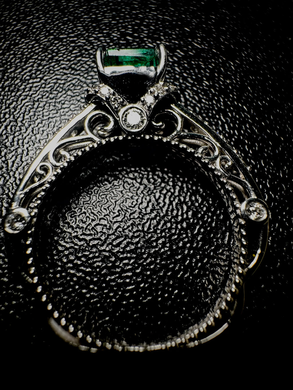 Platinum ring with a green gemstone on a textured black surface