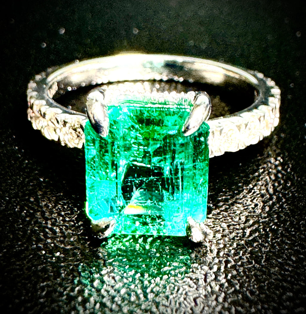 Platinum and diamond ring with a green gemstone on a dark background